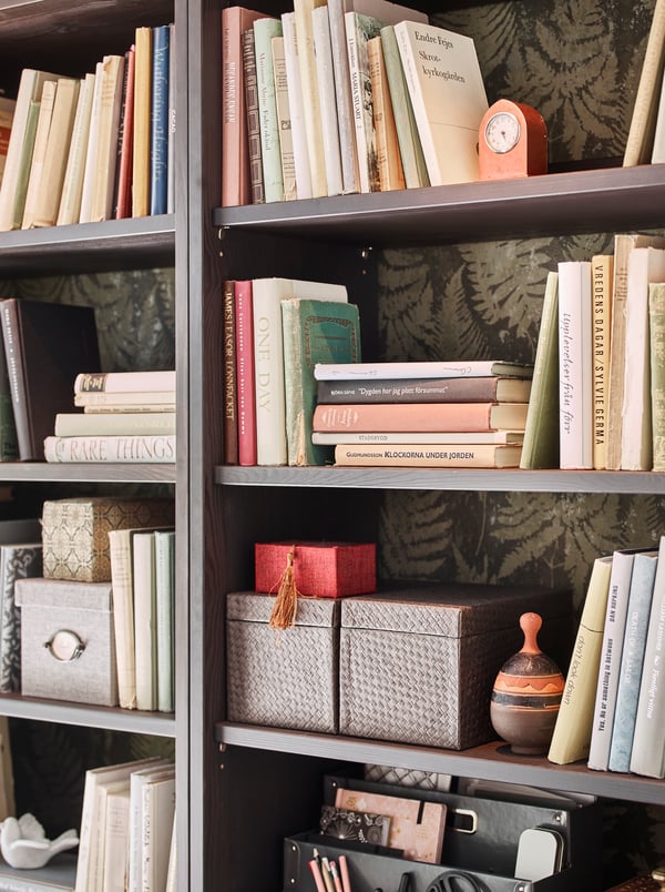 HAVSTA dark brown storage cabinets with four open shelves, leafy wallpaper, books and boxes stored on the shelves.