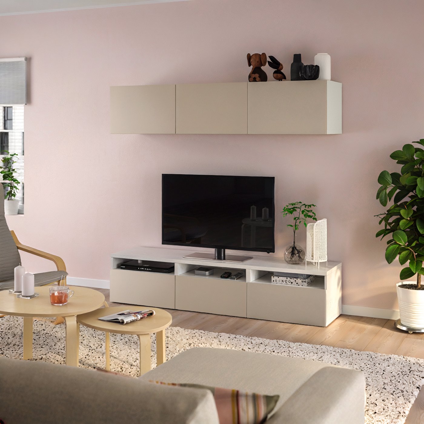 Composizione soggiorno con mobile TV BESTÅ beige, contro una parete rosa chiaro in un soggiorno con divano beige e tavolini da caffè.
