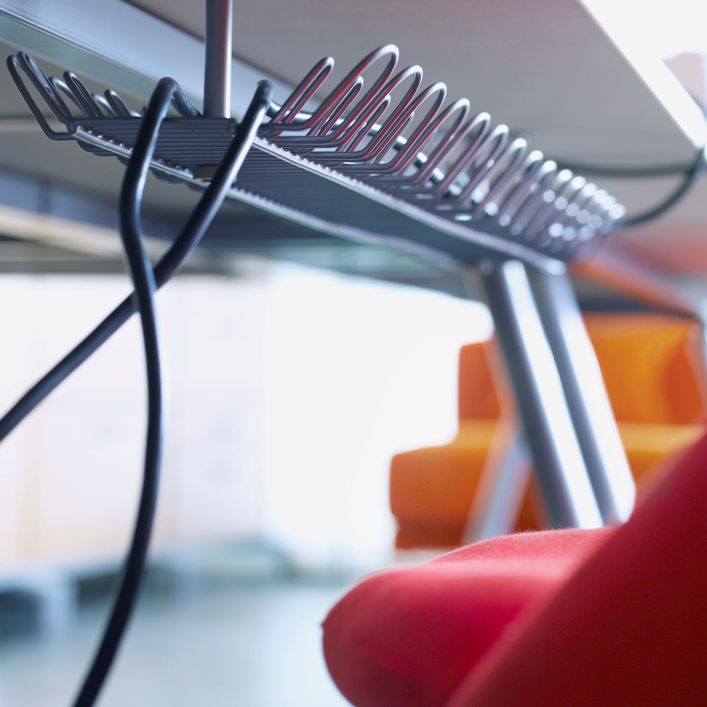 Två kablar kommer ut från änden av en SIGNUM kabelkanal horisontellt, som är fäst under ett skrivbord.