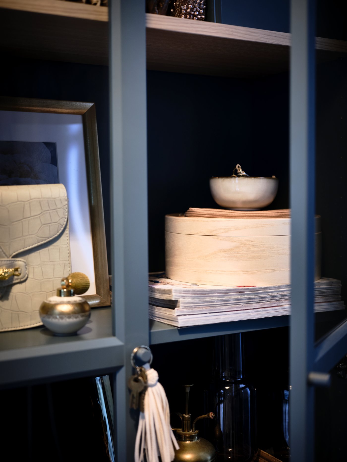 A section of a grey-turquoise BILLY glass-door bookcase with its shelves filled with frames, decorations and artful objects.