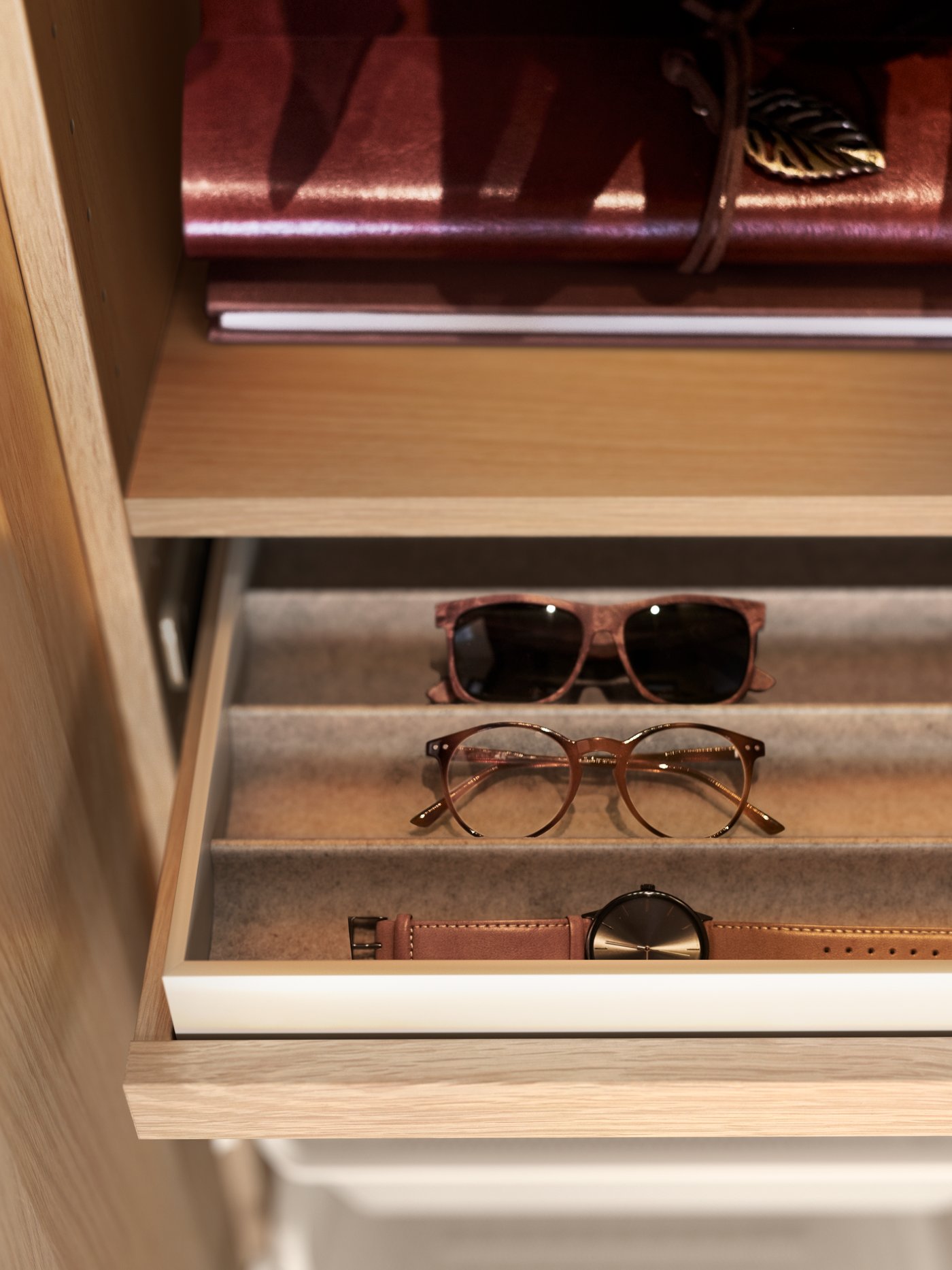 Detalle de un cajón de armario abierto con un accesorio de tela gris claro, con 4 compartimentos para guardar varios pares de gafas de sol.