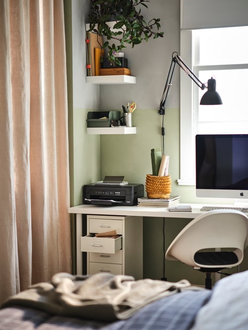 An office space in a bedroom with a LAGKAPTEN/ADILS desk and LOBERGET/MALSKÄR swivel chair with white LACK shelves above.