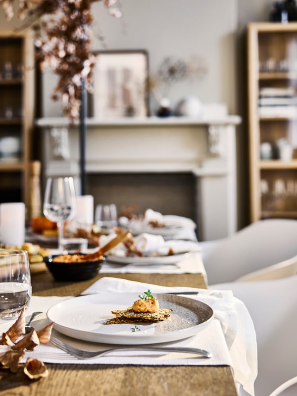A side view of an autumn-themed table setting with white table runners and set plates.