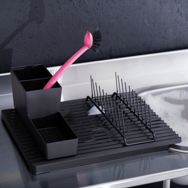Vue en angle d’un RINNIG porte-vaisselle noir et d’une simple brosse rose dans un support noir.
