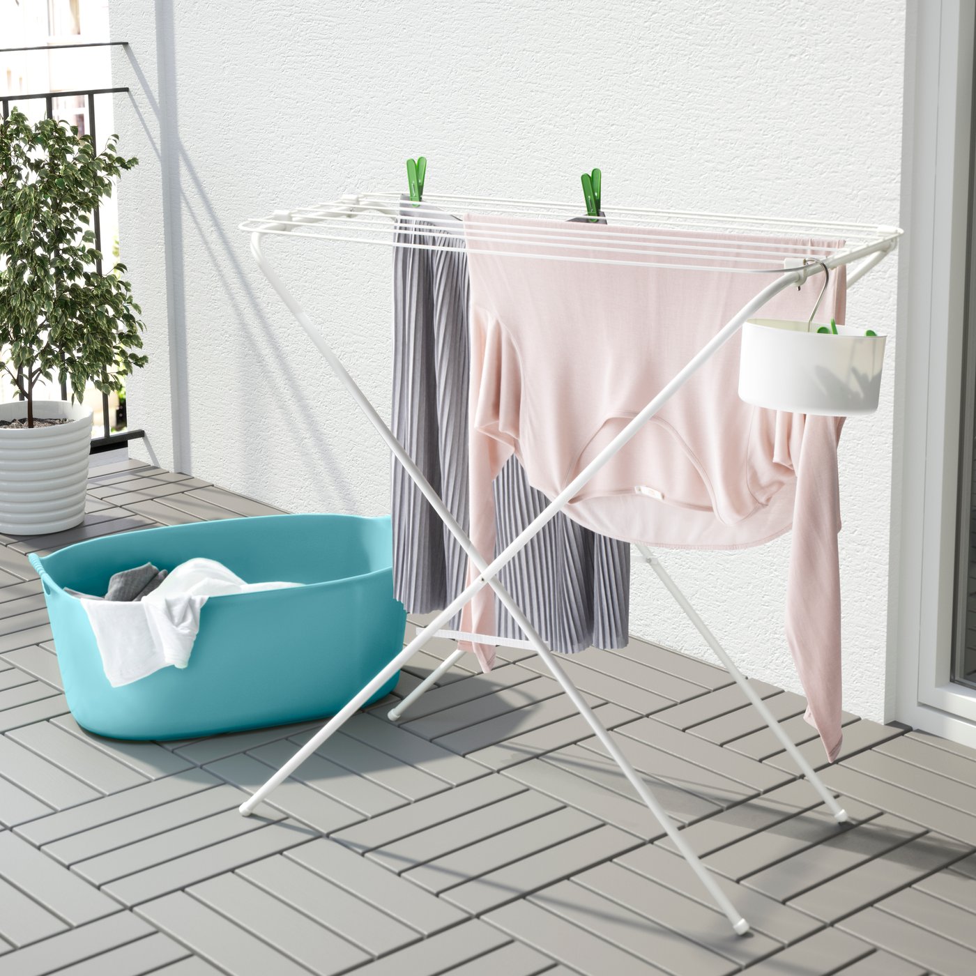 Tendedero JÄLL blanco con ropa colgada, colocado en un espacio al exterior. 