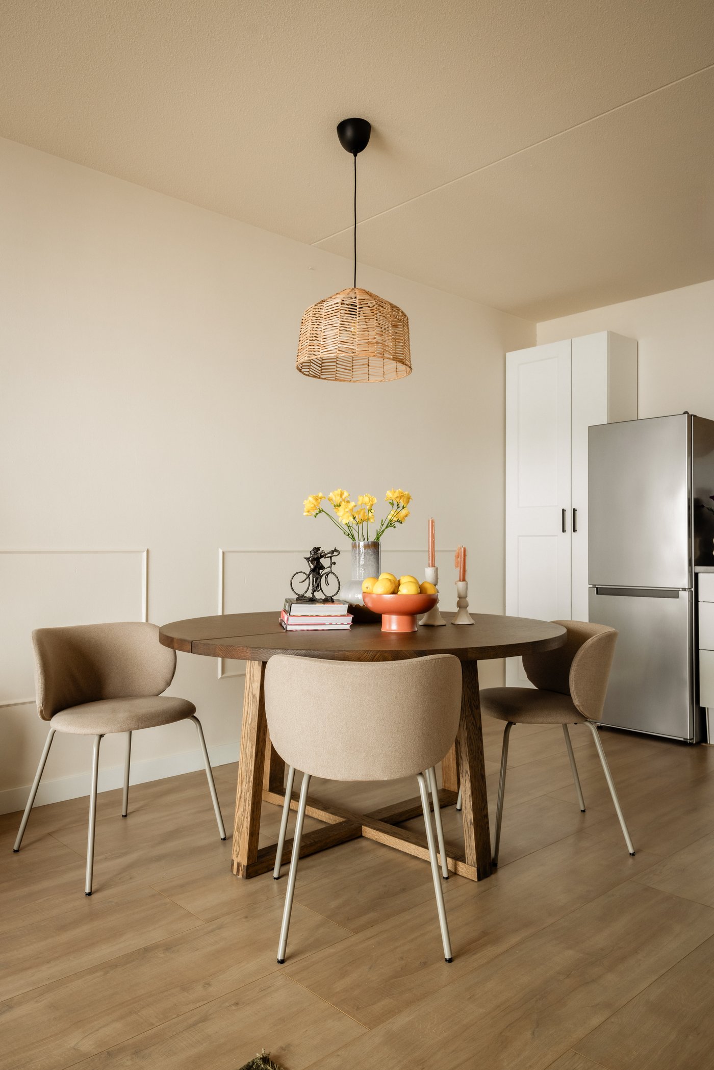 Eethoek met daarin een ronde eettafel van hout, met hier omheen vier beige KRYLBO eetkamerstoelen. Boven de tafel hangt een KAPPELAND / HEMMA rotan hanglamp.