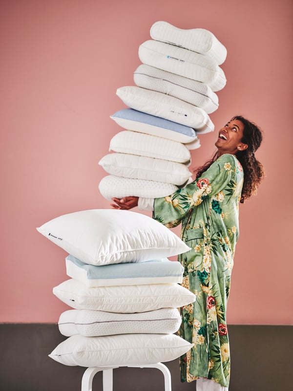 Une pile de coussin sur une chaise avec une femme à côté.