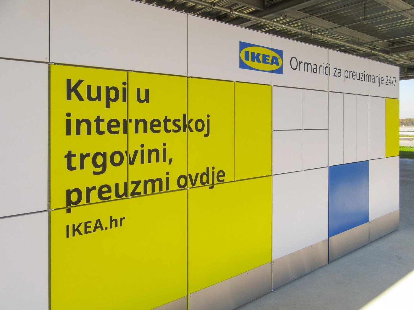 IKEA ormarići za preuzimanje 24/7; lijevo žuti panel s tekstom "Kupi u internetskoj trgovini, preuzmi ovdje IKEA.hr", desno bijeli i plavi ormarići.