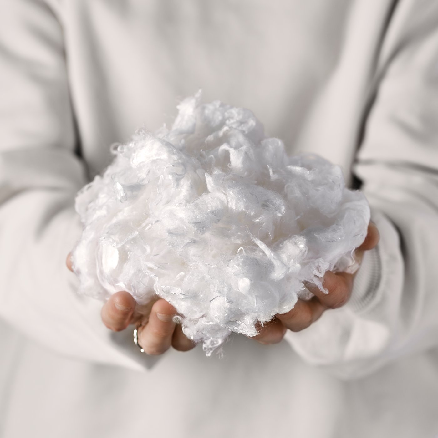 A close-up of two hands holding a white mass of lyocell fibres, which looks soft and fluffy.