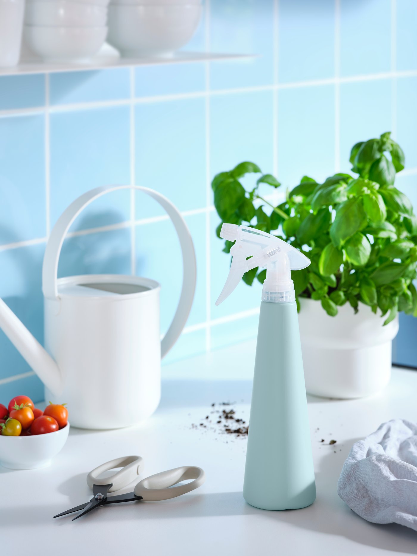 سطح مطبخ عليه إبريق سقي، وقنينة بخاخ ‪TOMAT‬، ومقص أعشاب ‪JACKFRUKT‬، وريحان ووعاء طماطم.