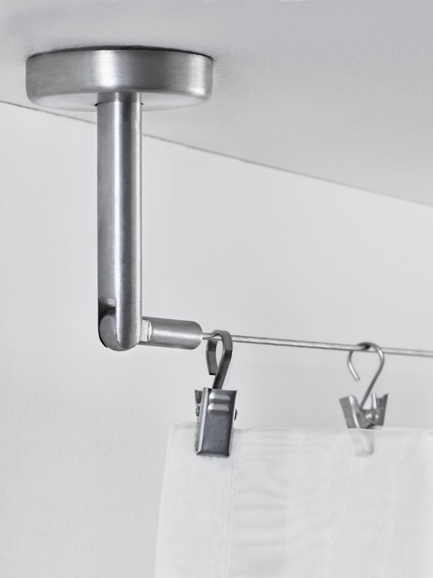 An einem Gardinenseilsystem hängen Haken und eine Gardine.