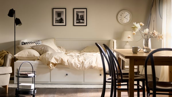 חדר בהיר עם שולחן אוכל מלפנים ומיטה נפתחת HEMNES מאחור. שתי תמונות ממוסגרות תלויות על הקיר מעל המיטה הנפתחת.