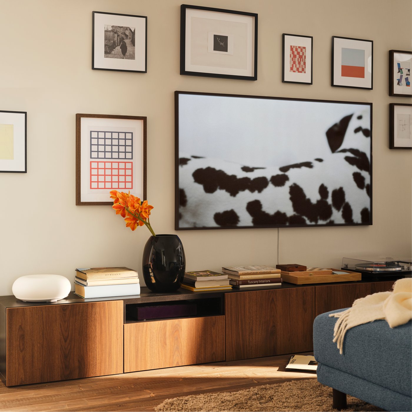 Two BESTÅ TV benches stand against a wall with a TV and pictures on it. A VARMBLIXT LED table/wall lamp stands on one bench.