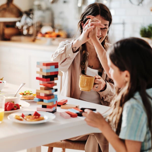 A mother and son high-five each other after successfully completing a block stacking game at the breakfast table.
