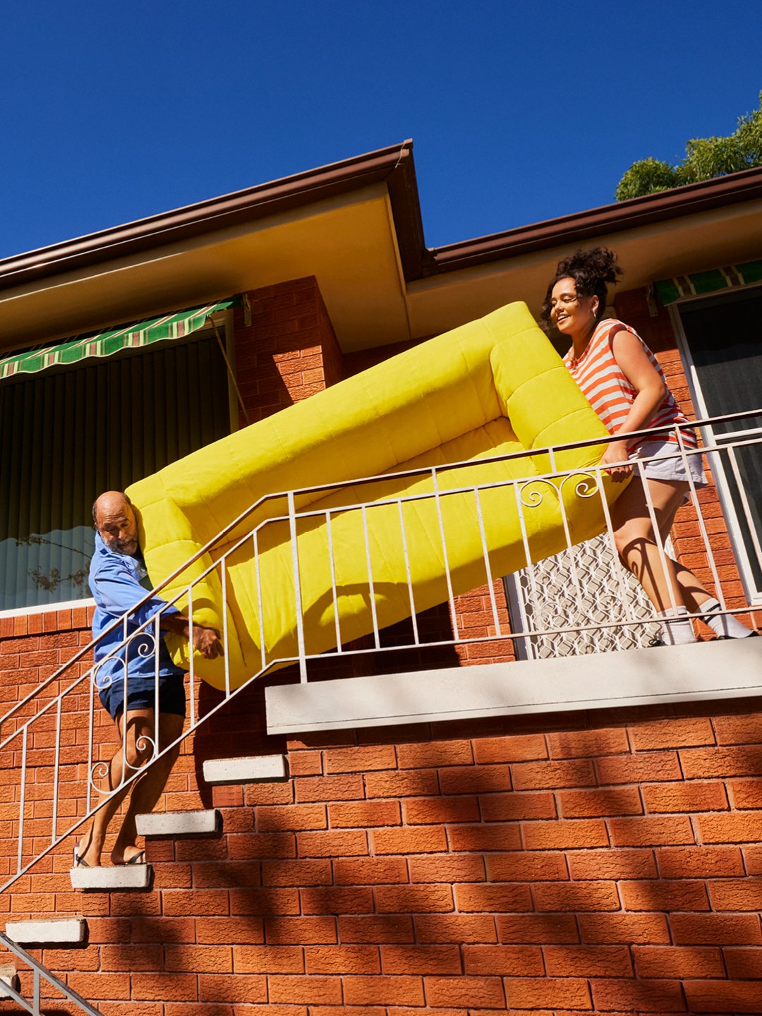 Father and daughter carrying a yellow KLIPPAN sofa