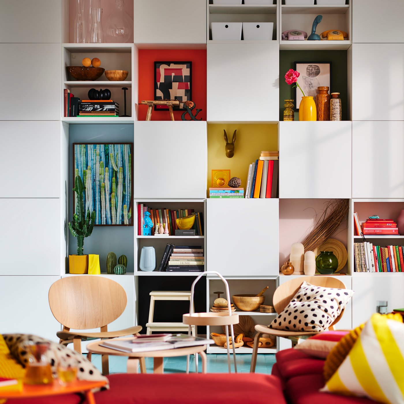 A living room with red sofas, pink walls and a white shelving system on the wall.