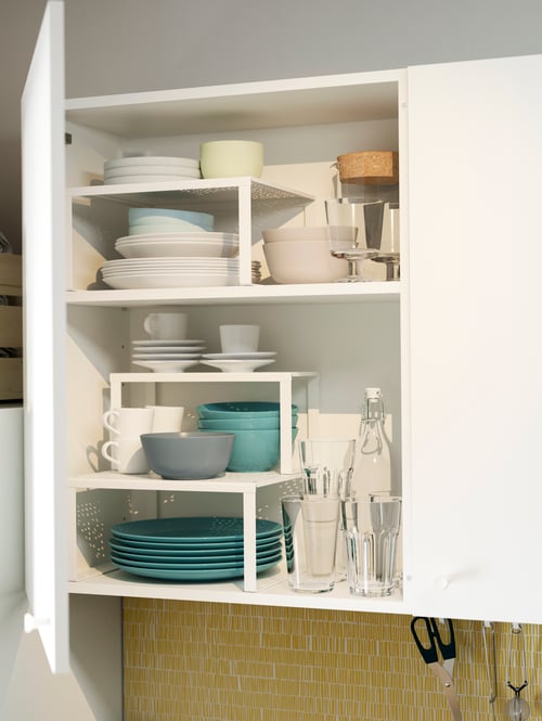 Küche mit einem zweitürigen, weißen Wandschrank mit zwei Türen. Hinter einer geöffneten Tür sind Regaleinsätze mit Tellern und Schüsseln zu sehen.