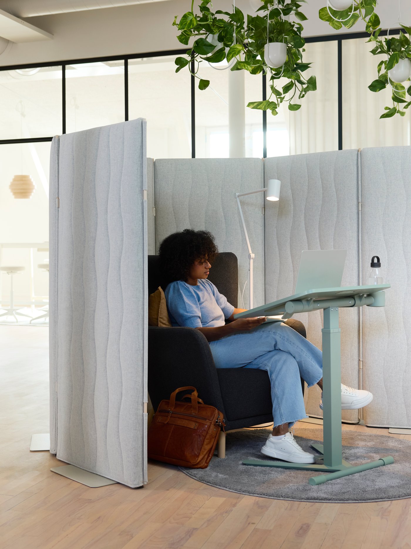 Person sitter i en avskärmad arbetsplats på kontor med ett laptopbord och hängande växter ovanför.