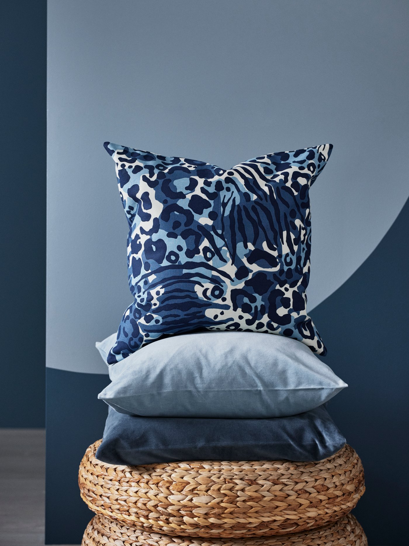 Una torre de cojines en tonos celestes y azules sobre una base de mimbre.