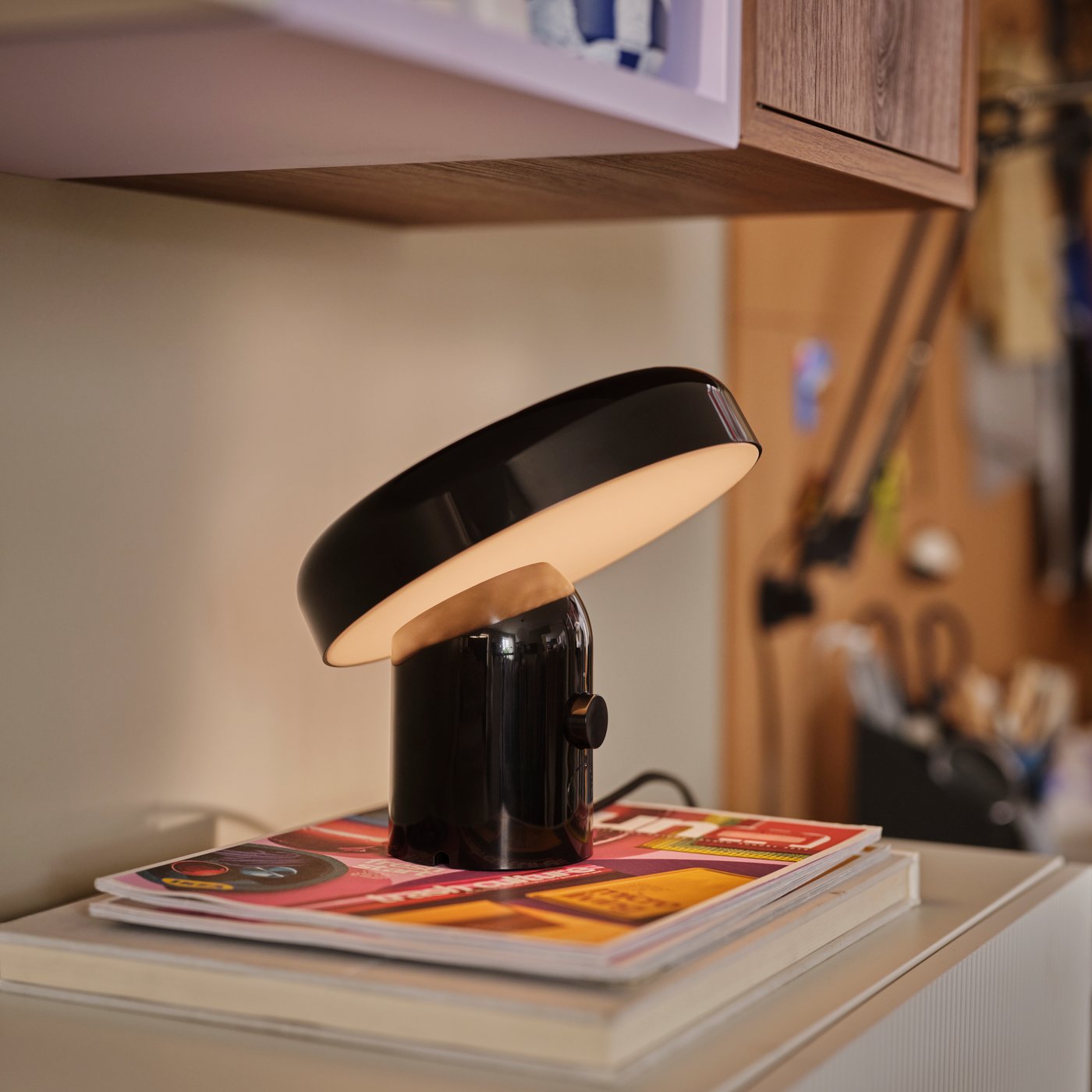 Part of a living-room wall with a lit, black BLOMPRAKT Bluetooth speaker lamp on top of a wall-mounted BESTÅ cabinet.