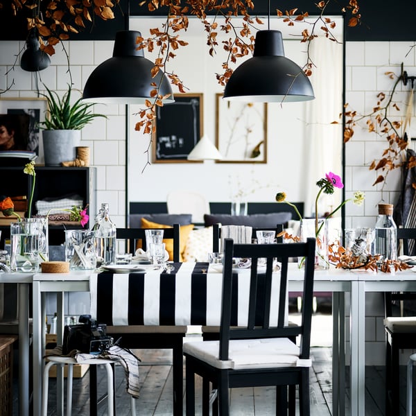 A decked-out black-and-white dining area with brown-black STEFAN chairs and MARIUS stools around two white MELLTORP tables.