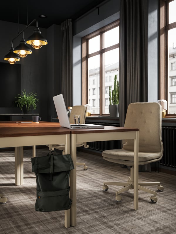 IDÅSEN brown/beige desks and MULLFJÄLLET chair, an olive-green backpack in the front and windows in the background.