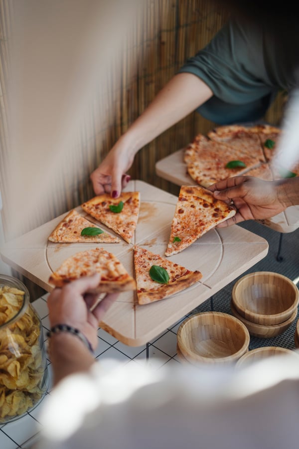 Persone che stanno prendendo fette di una pizza posta su un tagliere in legno SÅPÖRTMAL.