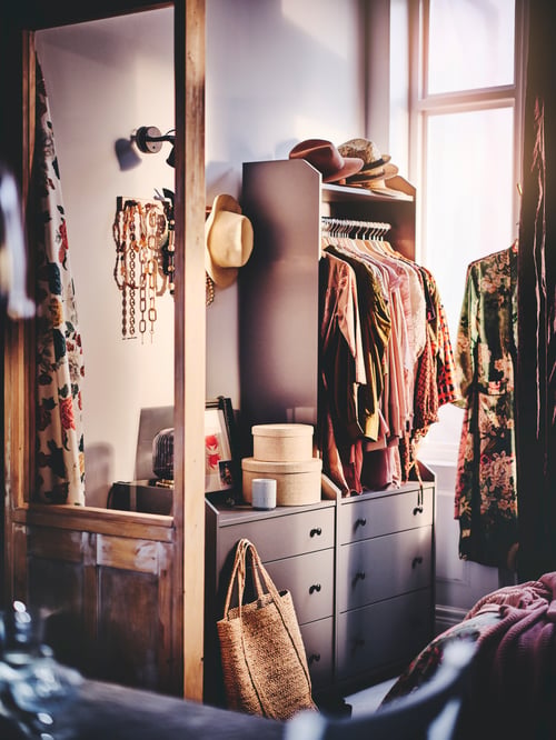 Hallway area featuring a grey chest of three drawers, and a grey open wardrobe with three drawers, containing clothes.