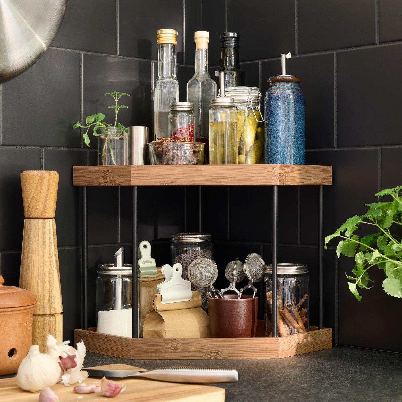 Una mensola angolare NÅLBLECKA con oggetti sul ripiano superiore e un ripiano inferiore da cui una persona prende delle bustine di tè e dei colini per tè.