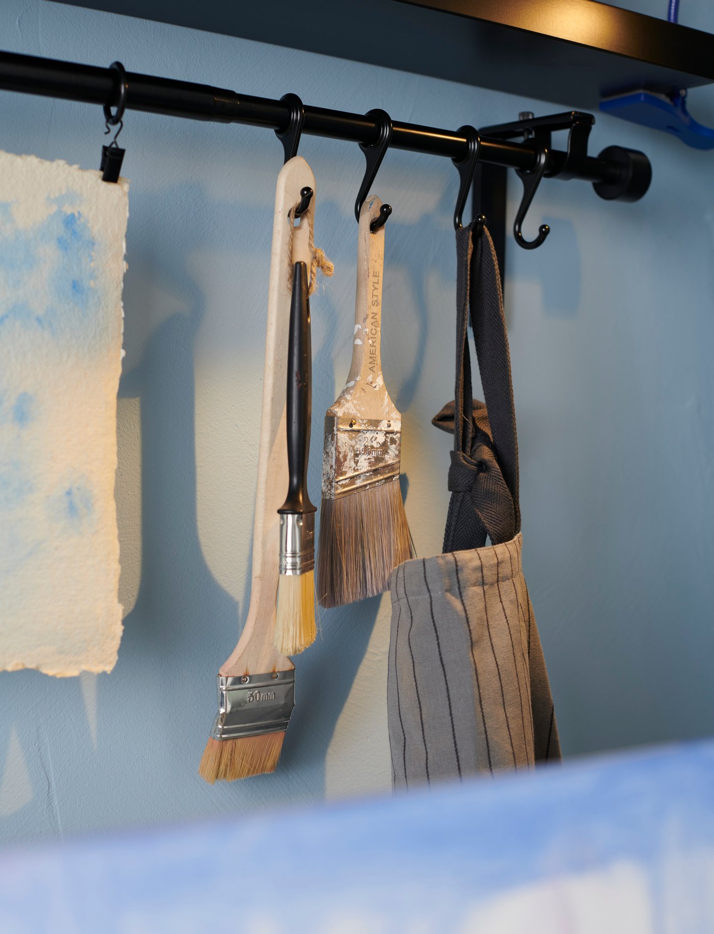 Barra para cortinas RÄCKA negras donde cuelgan pinceles.
