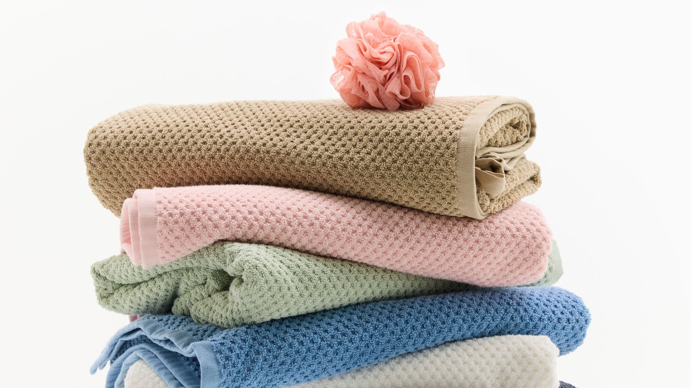 Toallas GULVIAL dobladas en diferentes colores, apiladas una sobre otra junto a una esponja de baño rosa.
