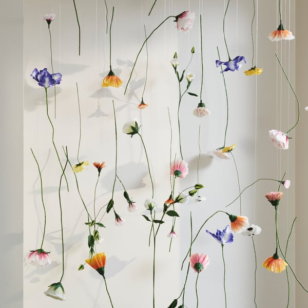 Mehrere GULDSPETT Kunstblumen hängen an unterschiedlich langen Fäden und bilden eine dekorative Hängedeko vor einer Wand.