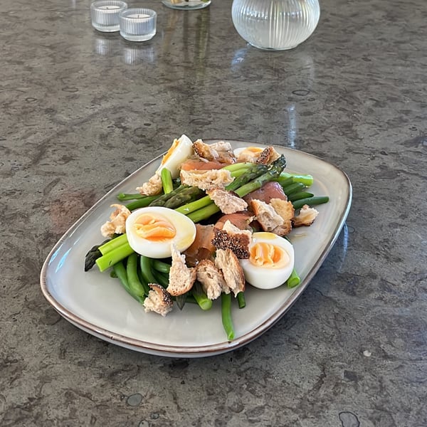 Laxsallad ligger upplagd på ett GLADELIG fat på ett grått bord.