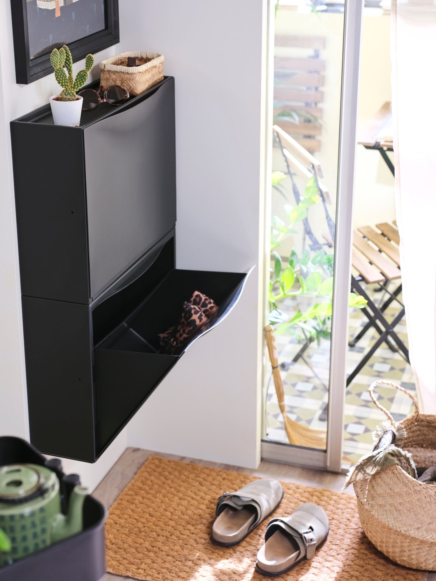 Two black plastic TRONES shoe cabinets/storage are on a wall by a sliding door that leads onto an enclosed balcony.