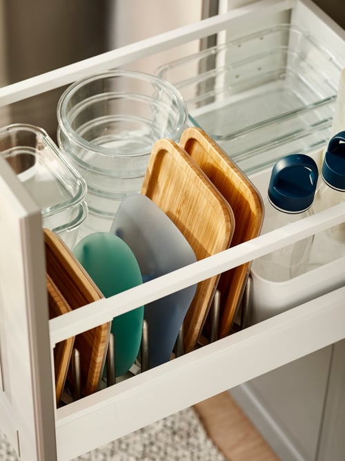Aproape de dulapul de bucătărie care conține multe recipiente alimentare din sticlă stivuite, capace din bambus, capace din plastic, sticle de apă din plastic.