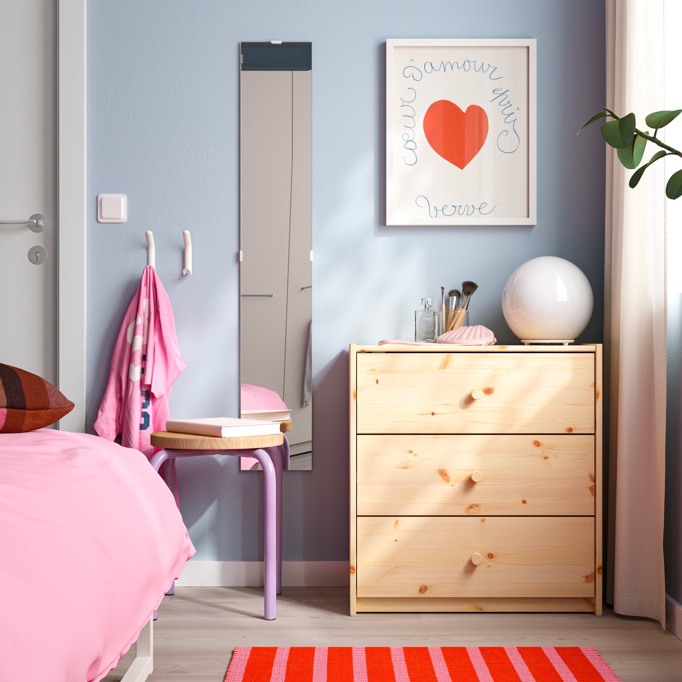 Espejo LÄRBRO colocado en la pared de un dormitorio, junto a una cómoda de madera y una cama con ropa de cama rosa.