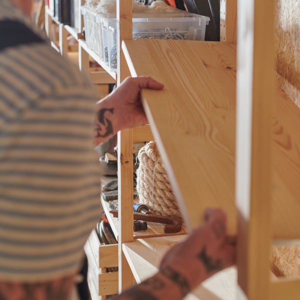 A person in a striped shirt is adding an IVAR shelf to an IVAR shelving unit.