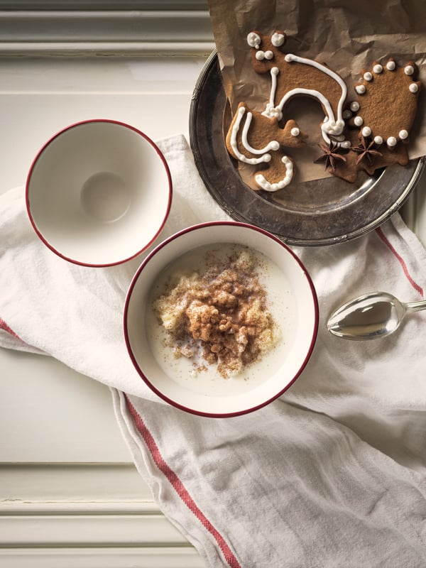 On a white surface is a spoon, a plate of gingerbread cookies, and two VINTER 2020 bowls, one containing oatmeal.
