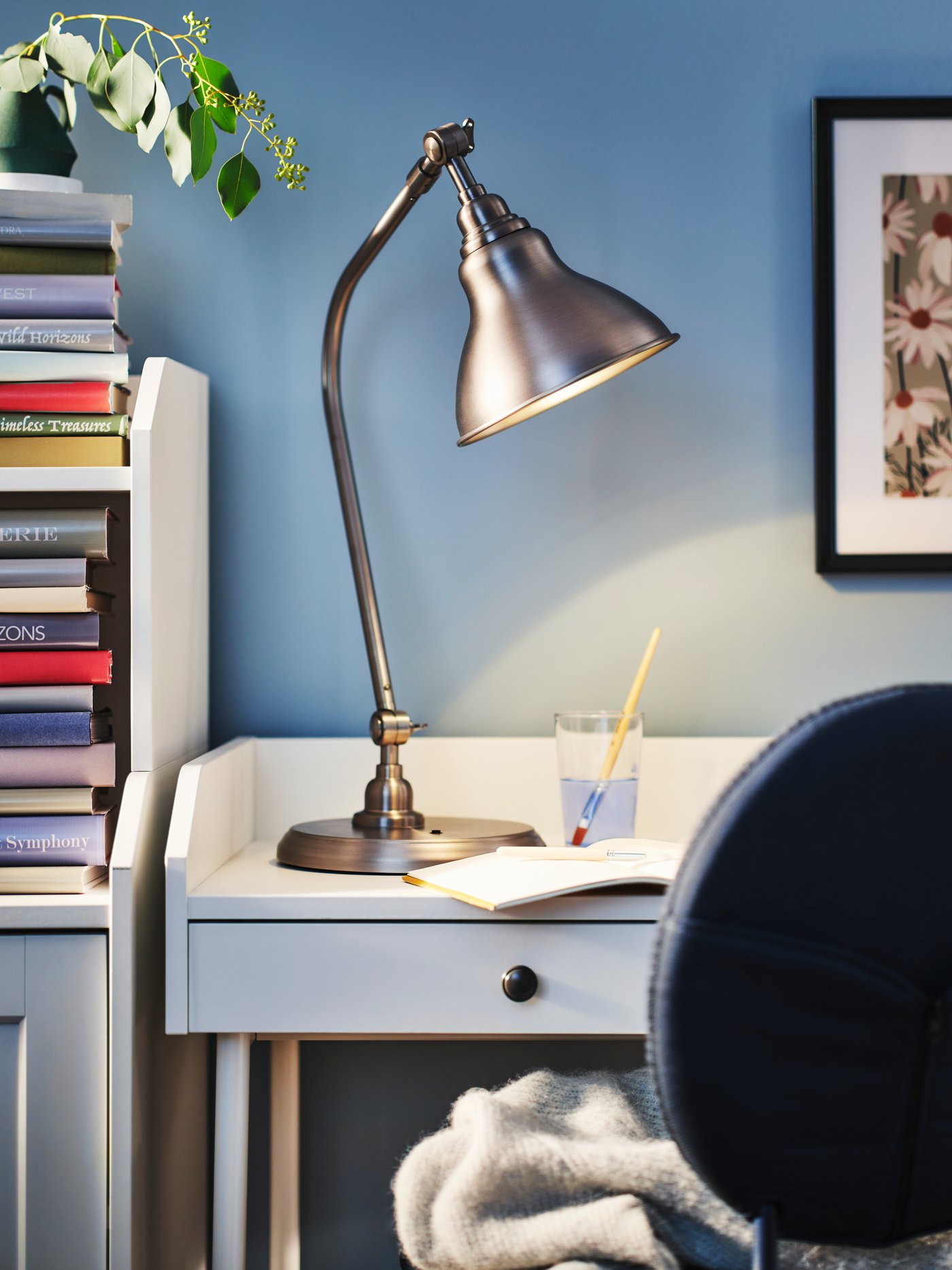 Eine ANKARSPEL Arbeitsleuchte in Zinneffekt steht auf einem weissen HAUGA Schreibtisch neben einem blauen BJÖRKBERGET Drehstuhl.