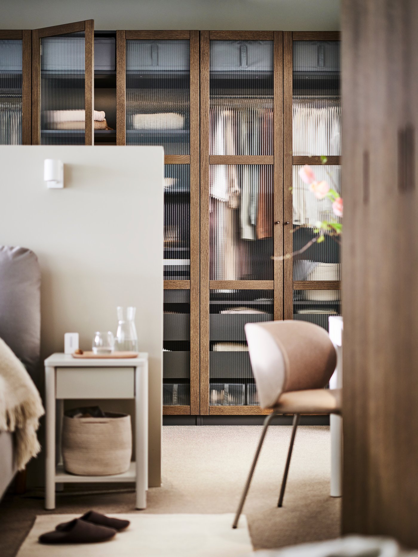 A dark grey brown/stained oak veneer glass PAX/TONSTAD wardrobe combination with a dark beige KRYLBO chair in front of it.
