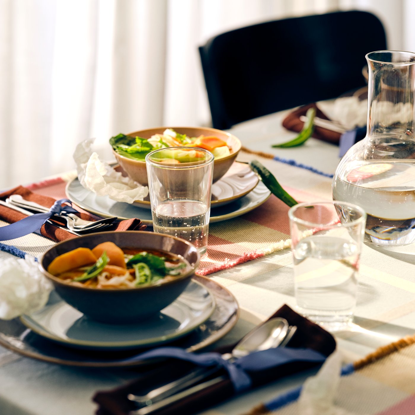 A table set in festive manner with FÄRGKLAR bowls and plates filled with diverse vegetables, glasses and tableware.