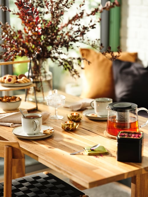 Modern kitchen featuring a table, a coffee and tea tin, a mug, a side plate, a vase, a teapot, and a tealight holder.