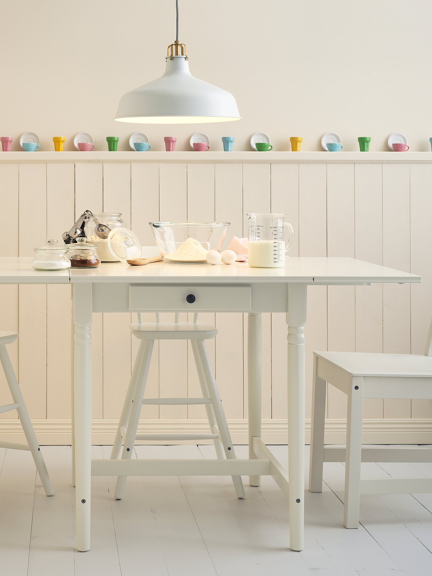 Comedor pequeño con mesa abatible INGATORP color balnco junto a un banco blanco.