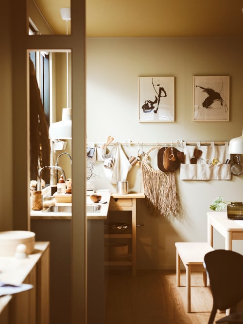 A kitchen setting with a FÖRHÖJA kitchen trolley. Above it,  a rail with a hanging organiser, a bag and wall decoration.