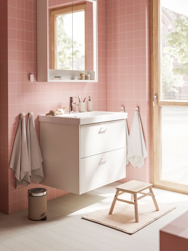 A white HAVBÄCK vanity with drawers and a mirror cabinet are placed in a bathroom with soft pink walls and a gray floor.