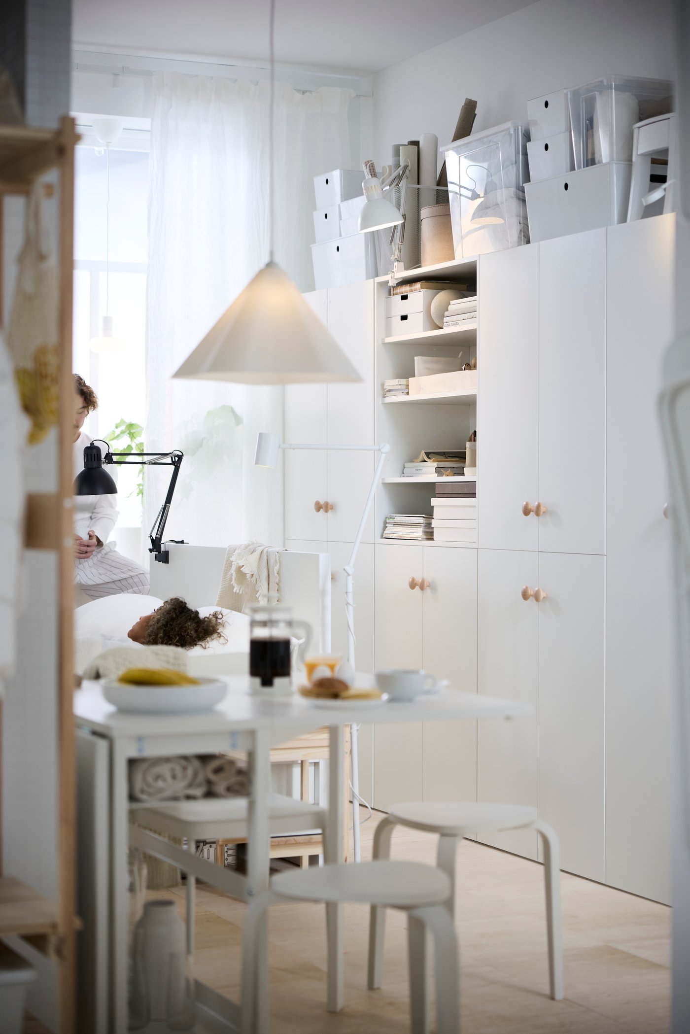 A multifunctional living space with white cabinets, a white bed frame and white table set with breakfast.