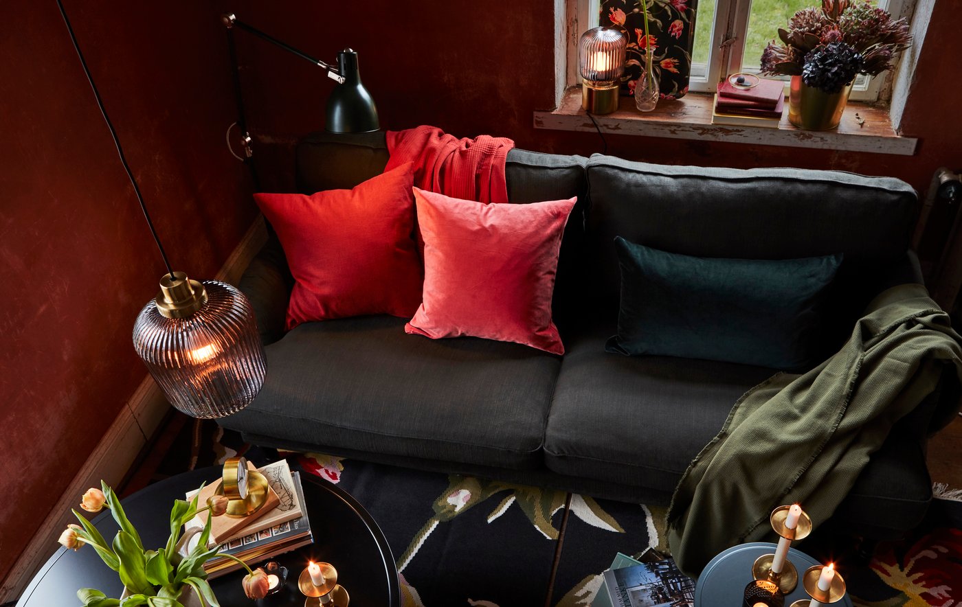Soggiorno con lampada a sospensione SOLKLINT, da terra e da tavolo, e un divano neri con cuscini rossi.