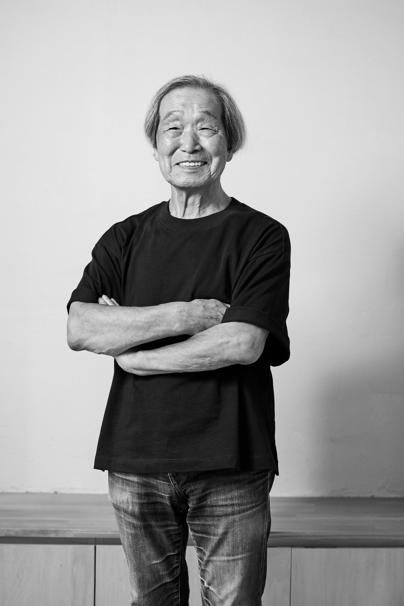 腕を組んで微笑む、デザイナー中村昇氏の白黒写真。