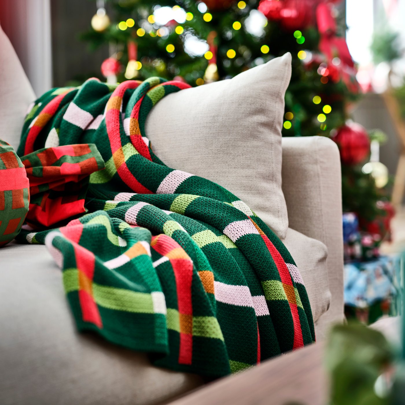 Un copridivano multicolore VINTERFINT su un divano beige davanti a un bellissimo albero di Natale.ree