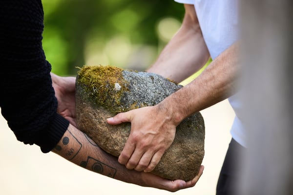 Two people passing each other a big stone.